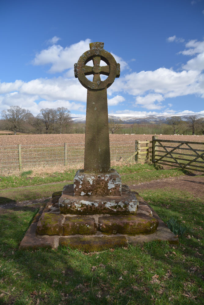 First view of the cross from the lane leading from Edenhall village to St. Cuthbert's Church.  The River Eden runs 250 metres east of the cross. St. Cuthbert's church is 230m south east of the cross.  The base looks very old, whereas the cross and shaft and head look as if they have been newly made, even though they were placed here in the 19th century.